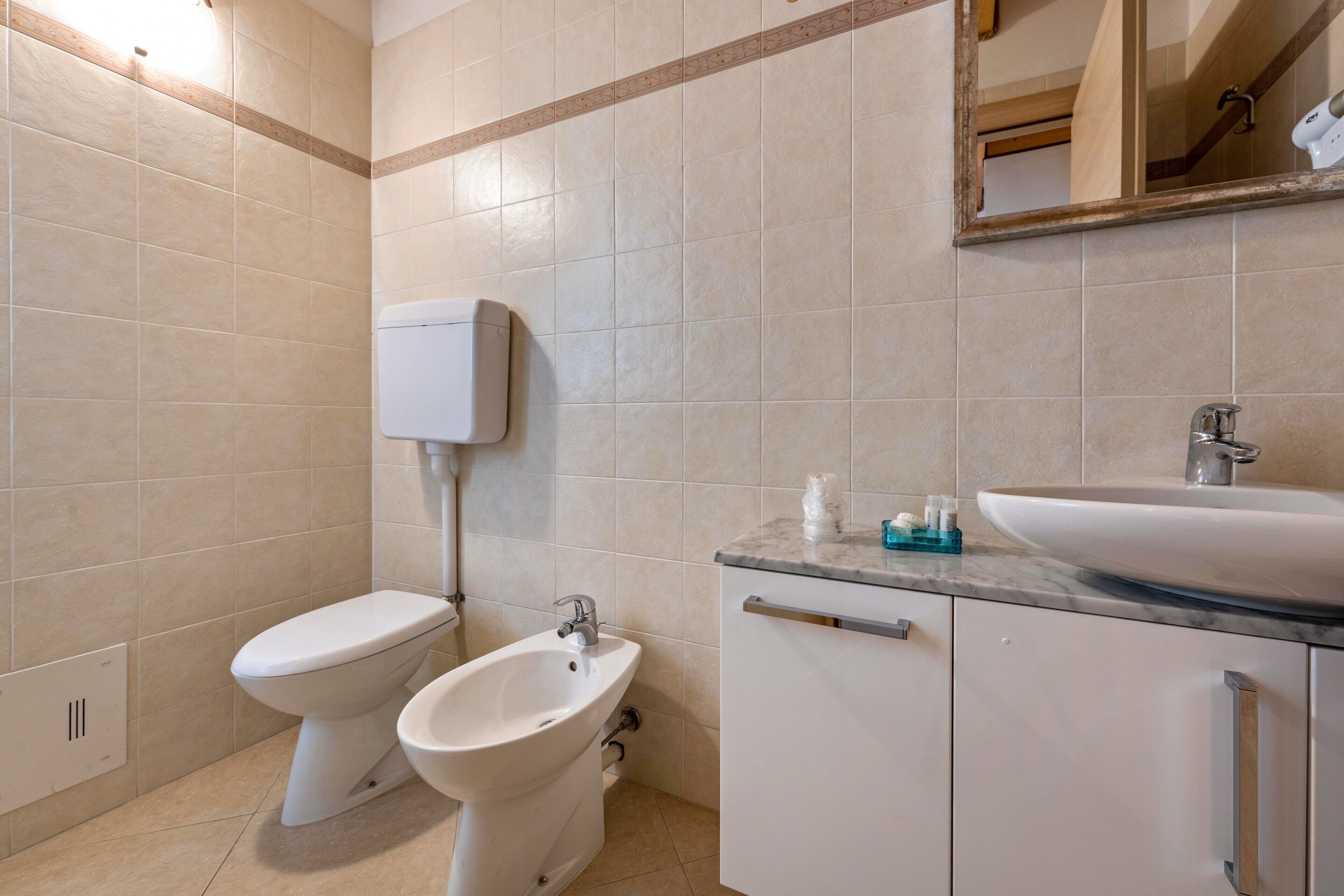 A bathroom with a toilet, bidet, sink, and cabinet.