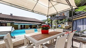 Un espace extérieur abrité comprenant une piscine, des meubles en osier et un pot de fleurs rouge.