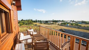 Eine Holzterrasse mit Sitzgelegenheiten und Blick auf Strand und Häuser in der Ferne.