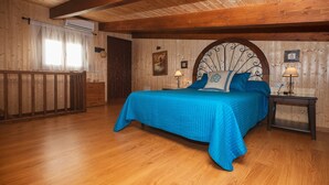 Ein Schlafzimmer mit Holzboden, einem Bett mit blauer Bettwäsche, einem Nachttisch mit Lampe und einem Fenster mit Vorhängen.