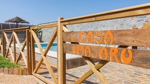 Ein Holzschild mit der Aufschrift 'CASA IMASARU', ein Holzzaun und ein Poolbereich.