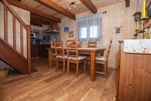 A wooden dining area with a table and chairs, a staircase, and a kitchen in the background.