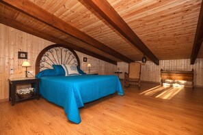 A bedroom with a wooden ceiling, a large bed with blue bedding, two bedside tables with lamps, and a wooden bench.