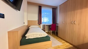 Ett litet sovrum med en säng, ett skrivbord, en stol och en garderob.