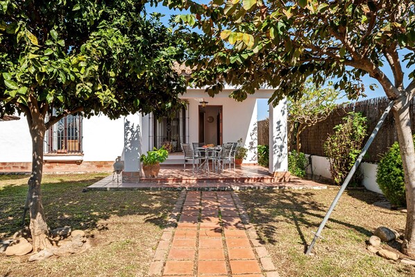 Une terrasse avec une table et des chaises, un petit jardin et un bâtiment doté d’une porte et de fenêtres.