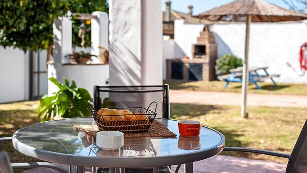 Une table en verre avec un panier d’oranges, une tasse blanche et une tasse rouge.