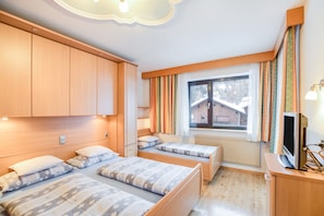 A room with two beds, a television, and a window with curtains.
