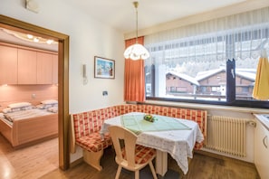 A cozy room with a bed, a dining table, a bench, and a window with a view of buildings.