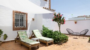 A patio with two wooden lounge chairs, a small table, and a potted plant. - Enjoy Conil: Near the Sea with Pool & Barbecue – Apartment C at Villa Mayo (Conil de la Frontera)