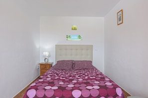Een slaapkamer met een bed, een nachtkastje, een lamp en twee afbeeldingen in een lijst op de muur.