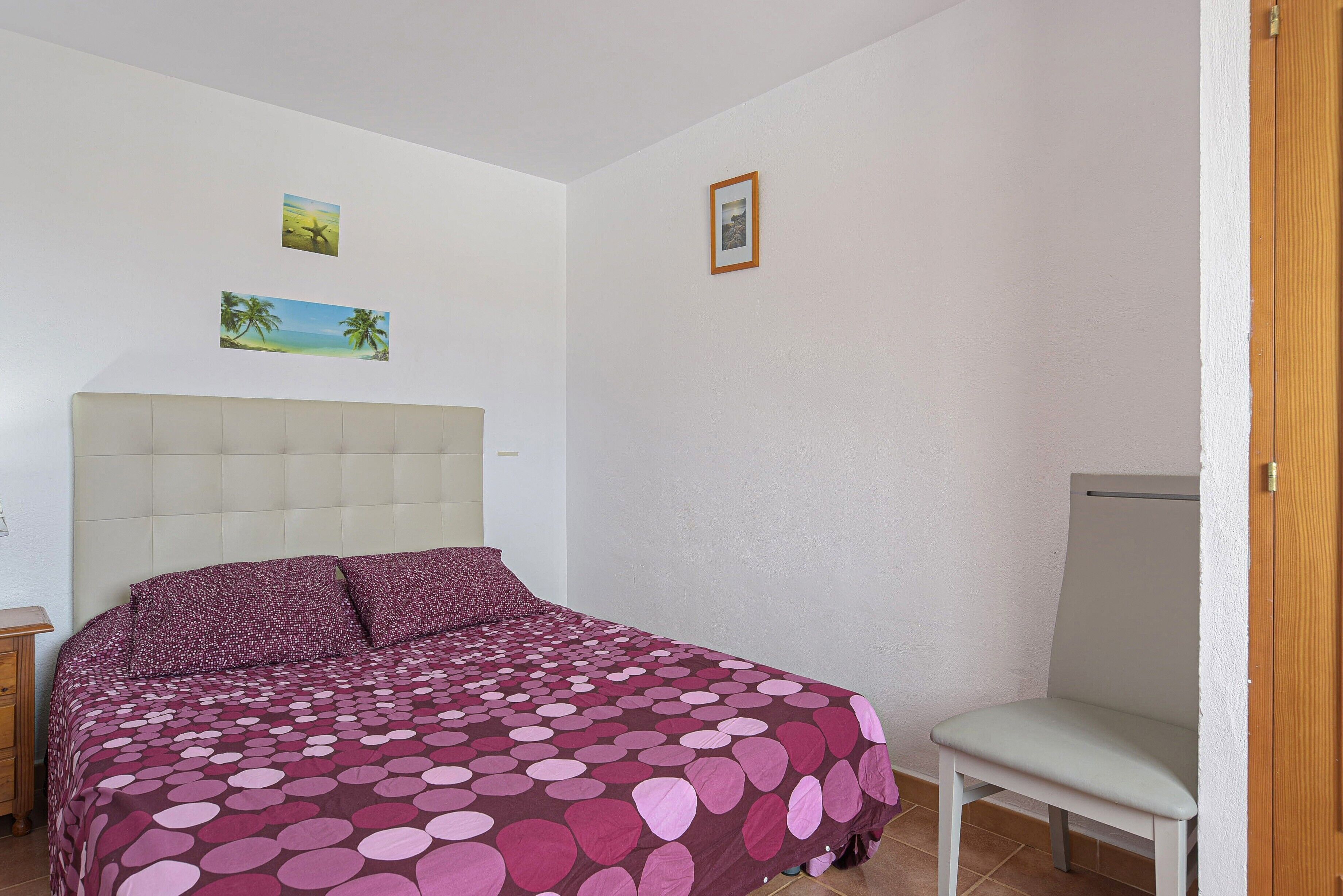 Un dormitorio con una cama, una silla y dos cuadros colgados en la pared.