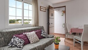 A living room with a sofa, a table with a potted plant, a dining area with a table and chairs, and a door leading to another room. - Enjoy Conil: Near the Sea with Pool & Barbecue – Apartment C at Villa Mayo (Conil de la Frontera)