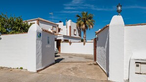 A white-walled building with a paved entrance, a palm tree, and a street lamp. - Enjoy Conil: Near the Sea with Pool & Barbecue – Apartment C at Villa Mayo (Conil de la Frontera)