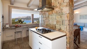 Una cocina con pared de piedra, estufa a gas, ventana con vistas y un comedor con mesa y sillas.