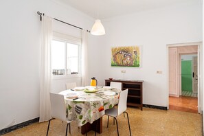 A dining area with a table set for four, a painting on the wall, and a view of the outside through a window.