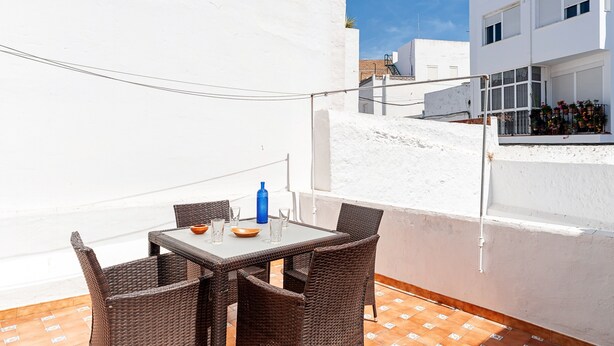 Un balcon avec une table et des chaises, une bouteille bleue et un bâtiment blanc en arrière-plan.