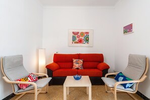 A room with a red sofa, two grey chairs, a small table, and a wall-mounted picture.