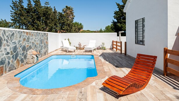 En swimmingpool med solstolar, en träbänk och en stenmur.
