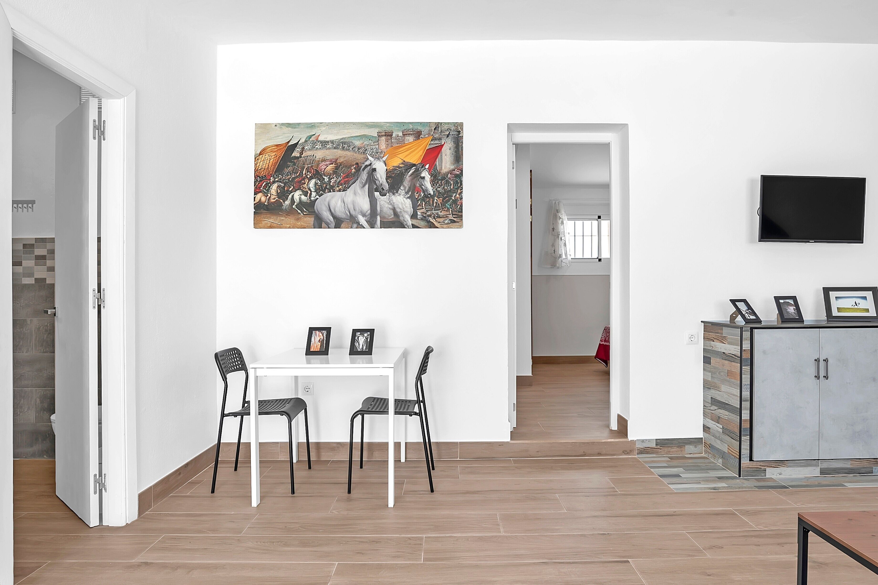 A modern living room with a dining area, a mounted TV, and a large painting on the wall.