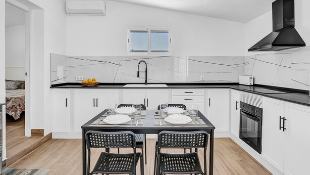 A modern kitchen with white cabinets, a black countertop, and a dining table set for four. - Comfortable Holiday Apartment "Loft Rural" with Terrace (El Soto)