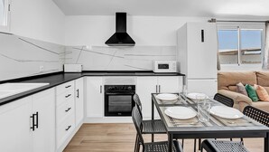 A modern kitchen with white cabinets, a black countertop, a built-in oven, and a dining area with a table set for two. - Comfortable Holiday Apartment "Loft Rural" with Terrace (El Soto)