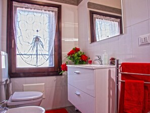 Ein Badezimmer mit Toilette, Waschbecken, Spiegel und roten Handtüchern.