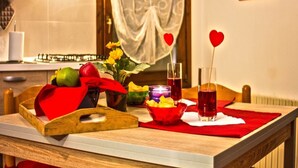 Una mesa de comedor con un posavasos rojo, un frutero, una vela y copas con adornos de corazón.