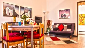 Un comedor con una mesa redonda, sillas y un sofá. Hay obras de arte en las paredes, una lámpara de pie y una planta en maceta.