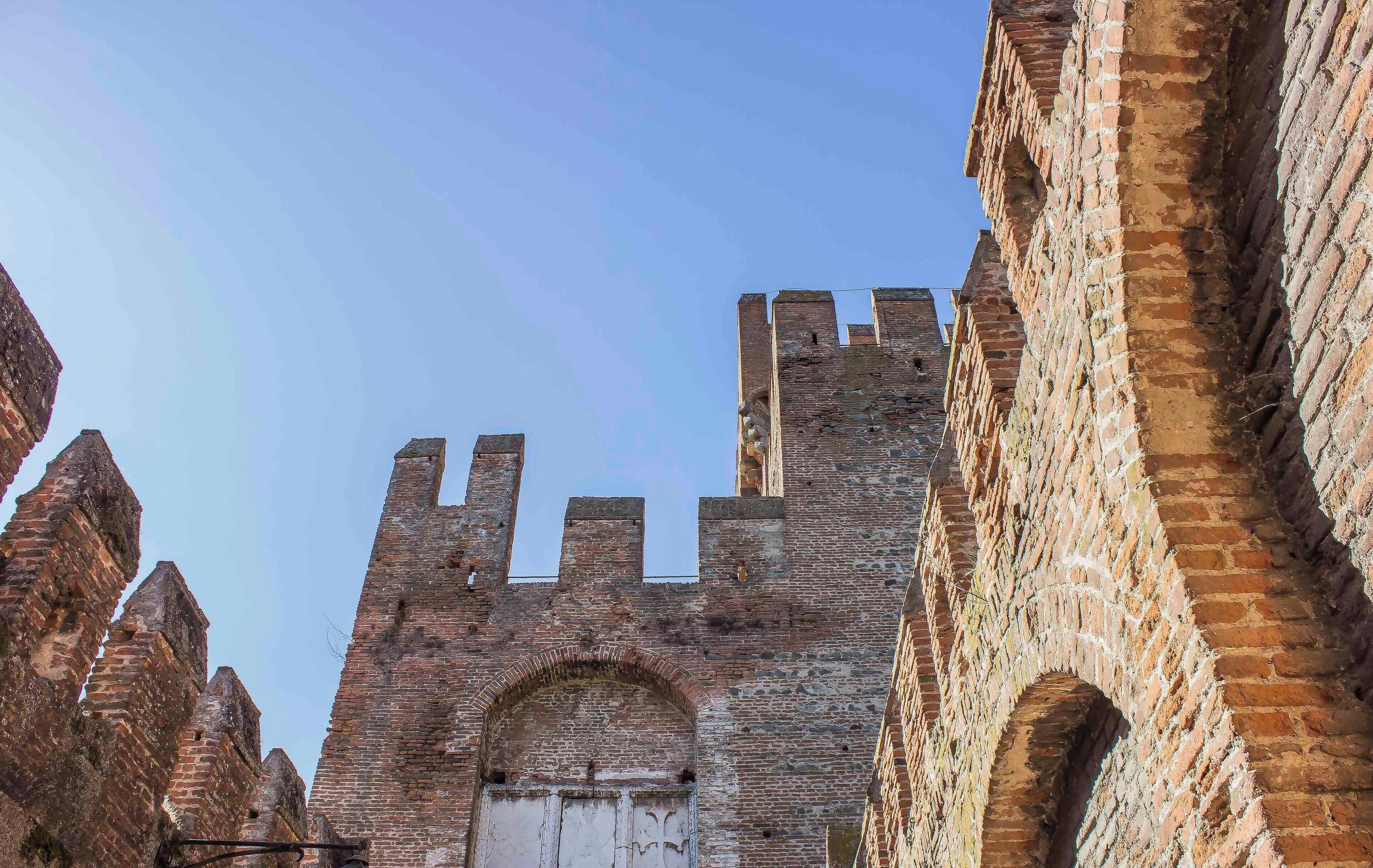 Un'antica torre in mattoni con finestre ad arco e un portale centrale, circondata da edifici simili.