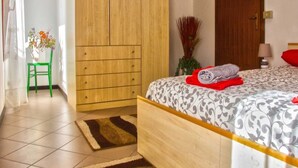 Un dormitorio con cama, armario de madera, una silla verde y un jarrón con flores.