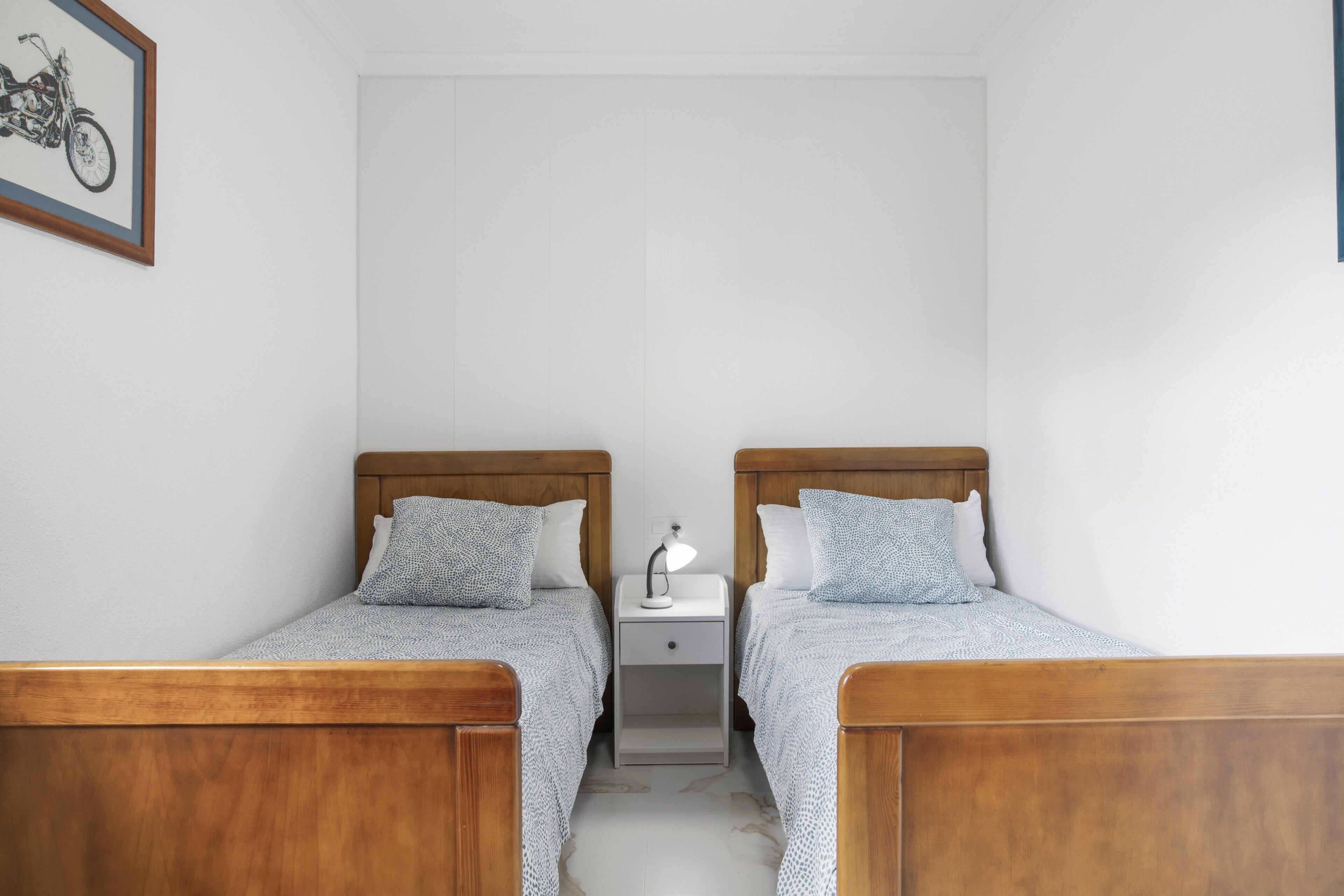 Une chambre à coucher avec deux lits en bois, une table de chevet avec une lampe et un tableau encadré au mur.