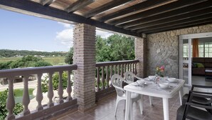 Une terrasse extérieure couverte, avec une table dressée pour les repas, un mur en pierre et une vue sur la campagne.