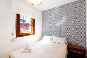 Un dormitorio con cama, ventana, pared con diseño y mesita de noche de madera.