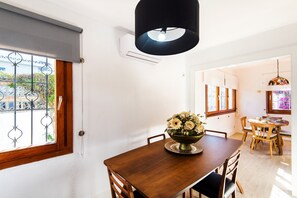 Un comedor con una mesa de madera, sillas, un jarrón de flores y una lámpara colgante negra.