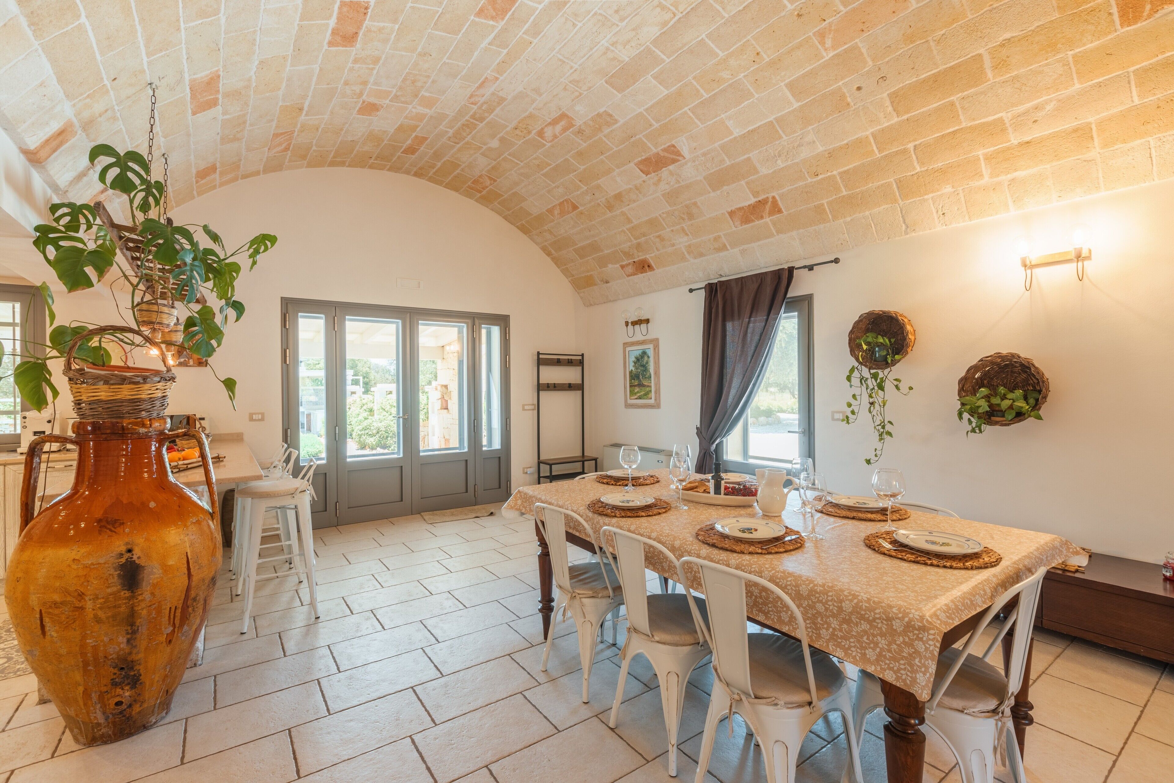 Un coin repas avec un plafond en briques, des chaises blanches, un grand vase et une table dressée pour le repas.