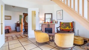 A living room with a fireplace, a dining table with chairs, a staircase, and a view of a hallway. - Sunny Lodge by Interhome (Cabourg)