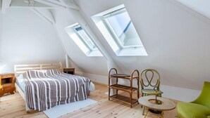 A bedroom with a sloped ceiling, a bed with striped bedding, a wooden nightstand, a green chair, and a small round table. - Sunny Lodge by Interhome (Cabourg)