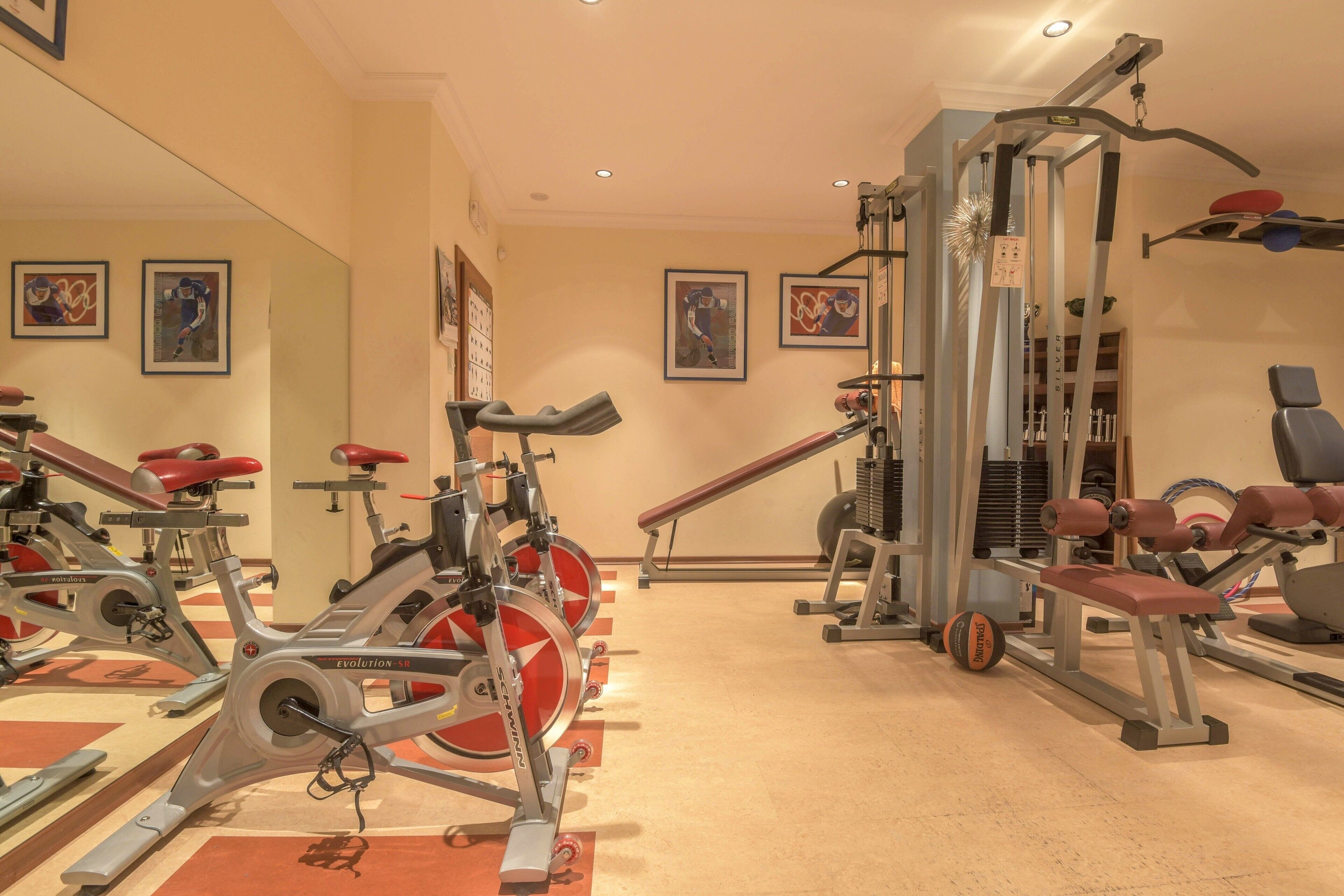 Een sportschool met hometrainers, een krachttrainingapparaat en een bank.