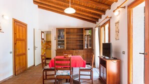 A dining area with a wooden ceiling, a red table, and chairs. There is a wooden cabinet with glass doors and a television on a stand. - Quietly Situated Holiday Home with Sea View, Garden & Terrace (Arzachena)