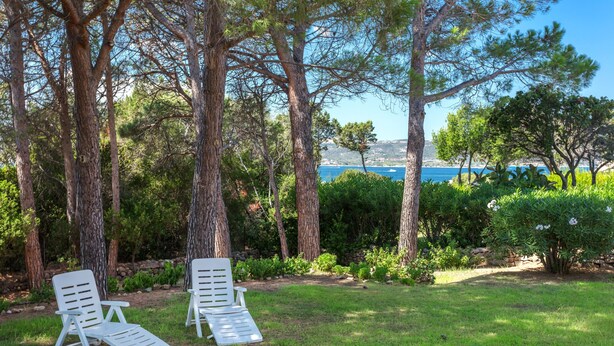 Two white lounge chairs in a grassy area with trees and a view of the sea. - Quietly Situated Holiday Home with Sea View, Garden & Terrace (Arzachena)