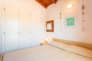 A bedroom with a bed, a nightstand with a lamp, a wooden ceiling, a door, and wall decorations.