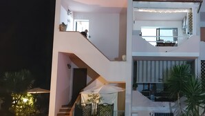Ein modernes, zweistöckiges Haus mit Treppe, Sitzgelegenheit im Freien und Blumentöpfen.