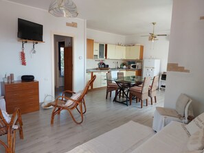 A modern living room with a dining area, kitchen, and a TV mounted on the wall.