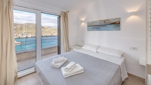 Hotelkamer met een bed, een schilderij, een nachtkastje en uitzicht op zee door een schuifdeur.