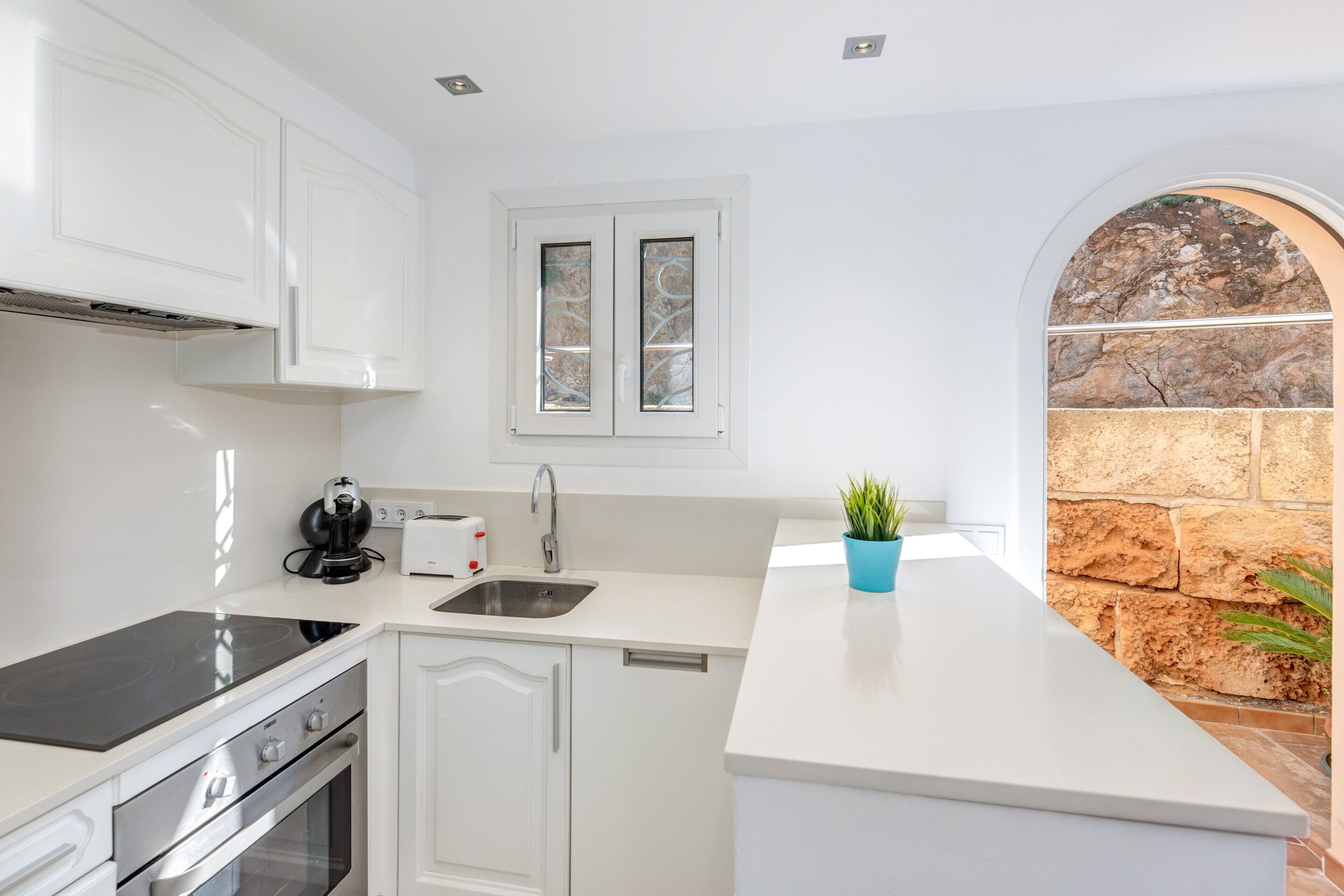 A modern kitchen with white cabinetry, a built-in oven, a stovetop, a sink, and a window with frosted glass.