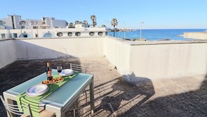 Terraza en la azotea con una mesa dispuesta para dos, con vistas a una zona costera con edificios y palmeras.
