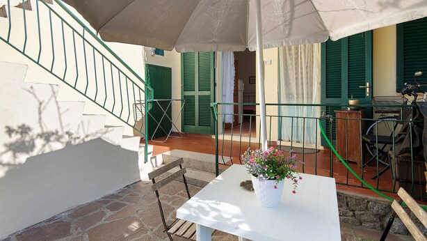 Un patio con una mesa blanca, una planta en maceta y un paraguas grande.