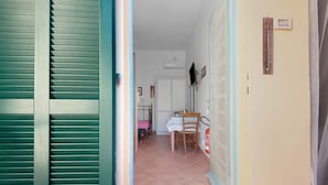 Un pasillo con una puerta cerrada, suelo de baldosas, una mesa y una silla, y un termómetro fijado a la pared.