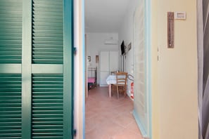 Un couloir avec une porte fermée, un sol carrelé, une table avec une chaise et un thermomÚtre fixé au mur.