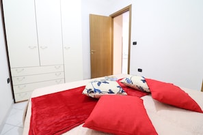 A bedroom with a bed, red pillows, a white wardrobe, and a wooden door.